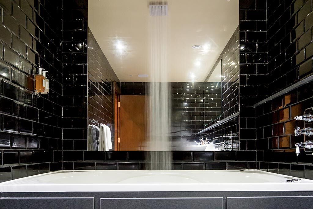 A modern bathroom with black tiled walls, a central shower, and a white bathtub.