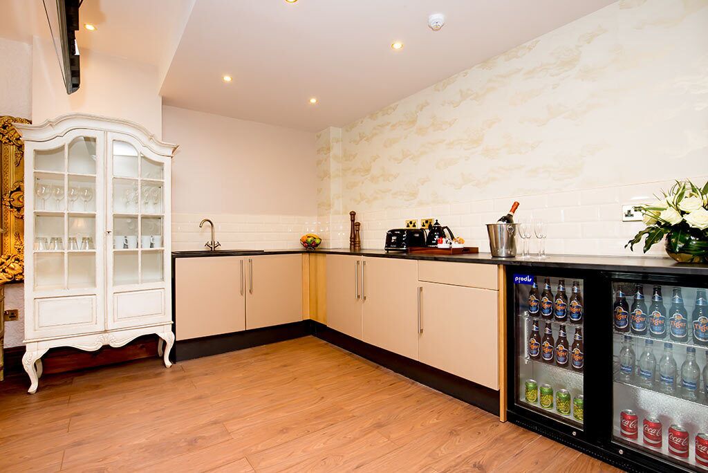 A modern kitchen with wooden cabinets, a built-in refrigerator stocked with beverages, and a decorative cabinet with glassware.