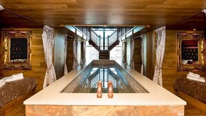 A long, narrow room with a central water feature, wooden walls, and a staircase leading to an upper level.