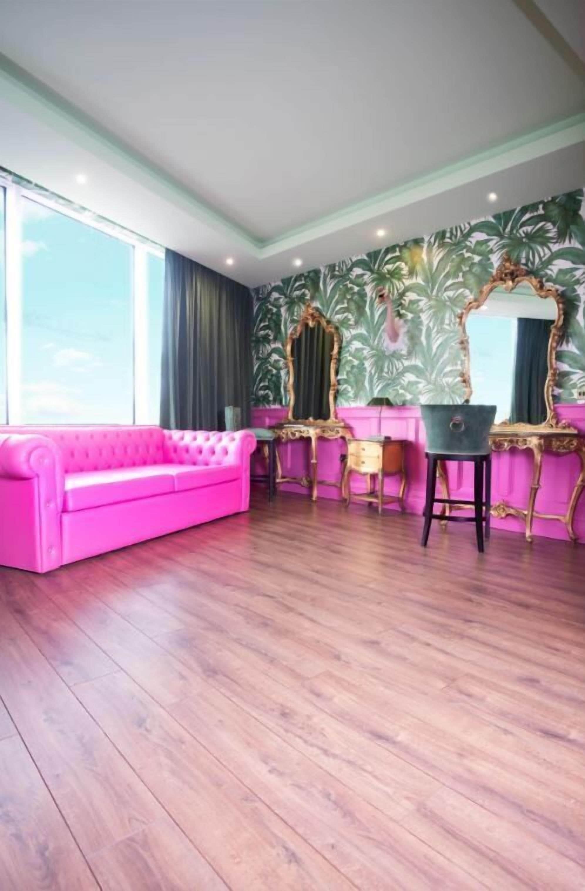 A room with a pink sofa, a vanity with a mirror, and a large window.