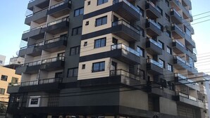 A multi-story residential building with balconies, a ground-level commercial space with signage, and a clear sky. - Guarapari Praia (Guarapari)