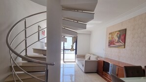 A modern interior with a spiral staircase, a dining area with a wooden table and chairs, and a living room with a sofa and a painting on the wall. - Guarapari Praia (Guarapari)