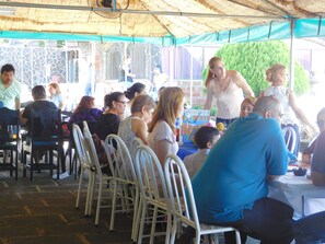 A covered outdoor seating area with metal chairs and tables, under a thatched roof.