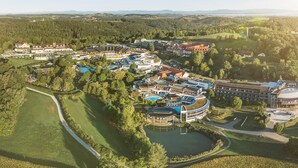 Ett flygbildsfoto av ett semesterområde med flera byggnader, en stor swimmingpool och omgivande grönska.