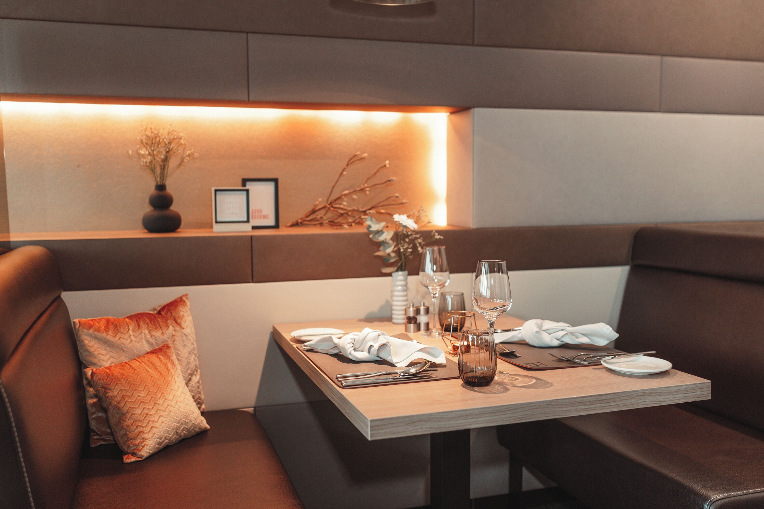 Un comedor con una mesa de madera dispuesta para dos personas, junto a un banco acolchado.