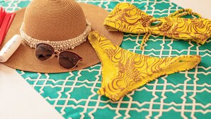 A bed with a patterned bedspread, a straw hat, sunglasses, and a yellow bikini on it. - Hotel Taybo Beach (Santa Marta)