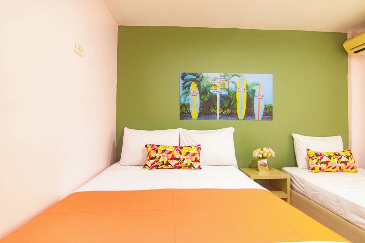Une chambre d’hôtel avec un grand lit, deux oreillers, une table de chevet ornée d’un vase de fleurs et un mur décoré d’un tableau sur le thème des pays tropicaux.