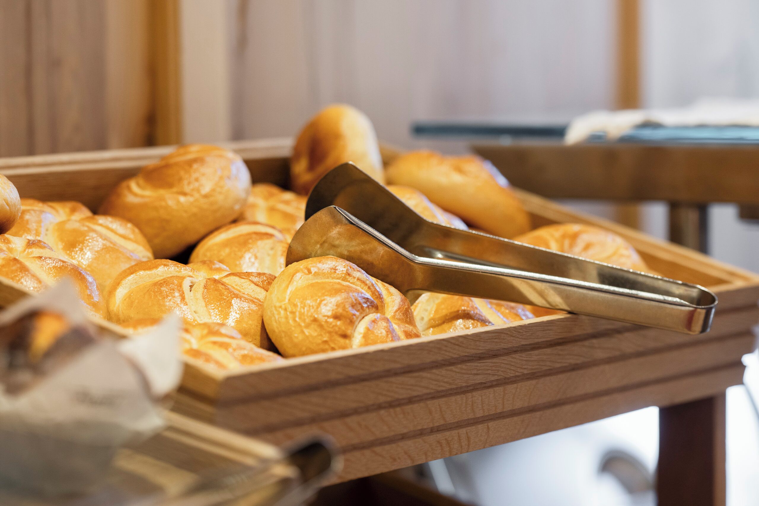 A wooden tray filled with golden-brown croissants and a metal spatula.