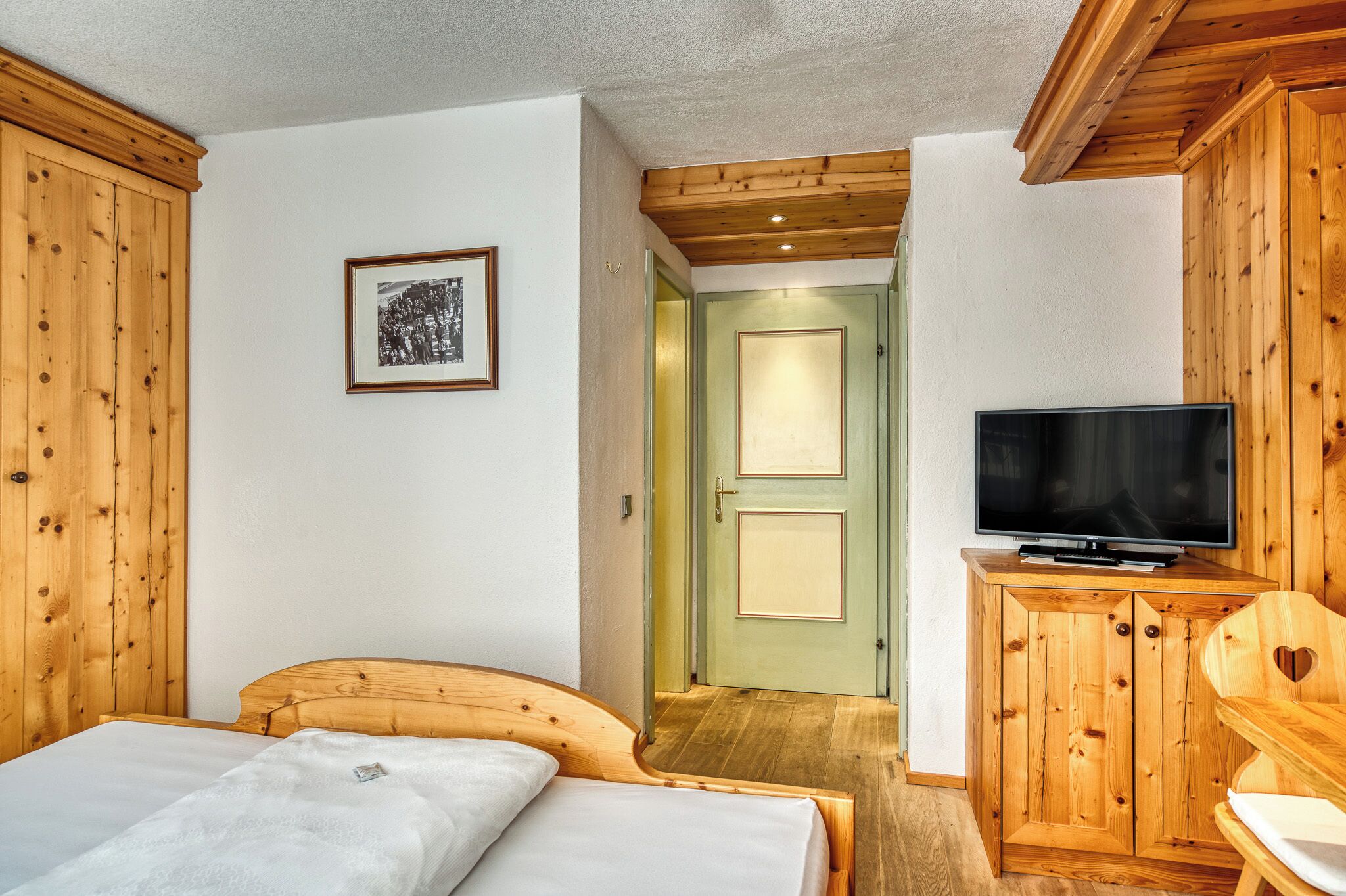 A wooden-paneled room with a bed, a television, and a door leading to another room.