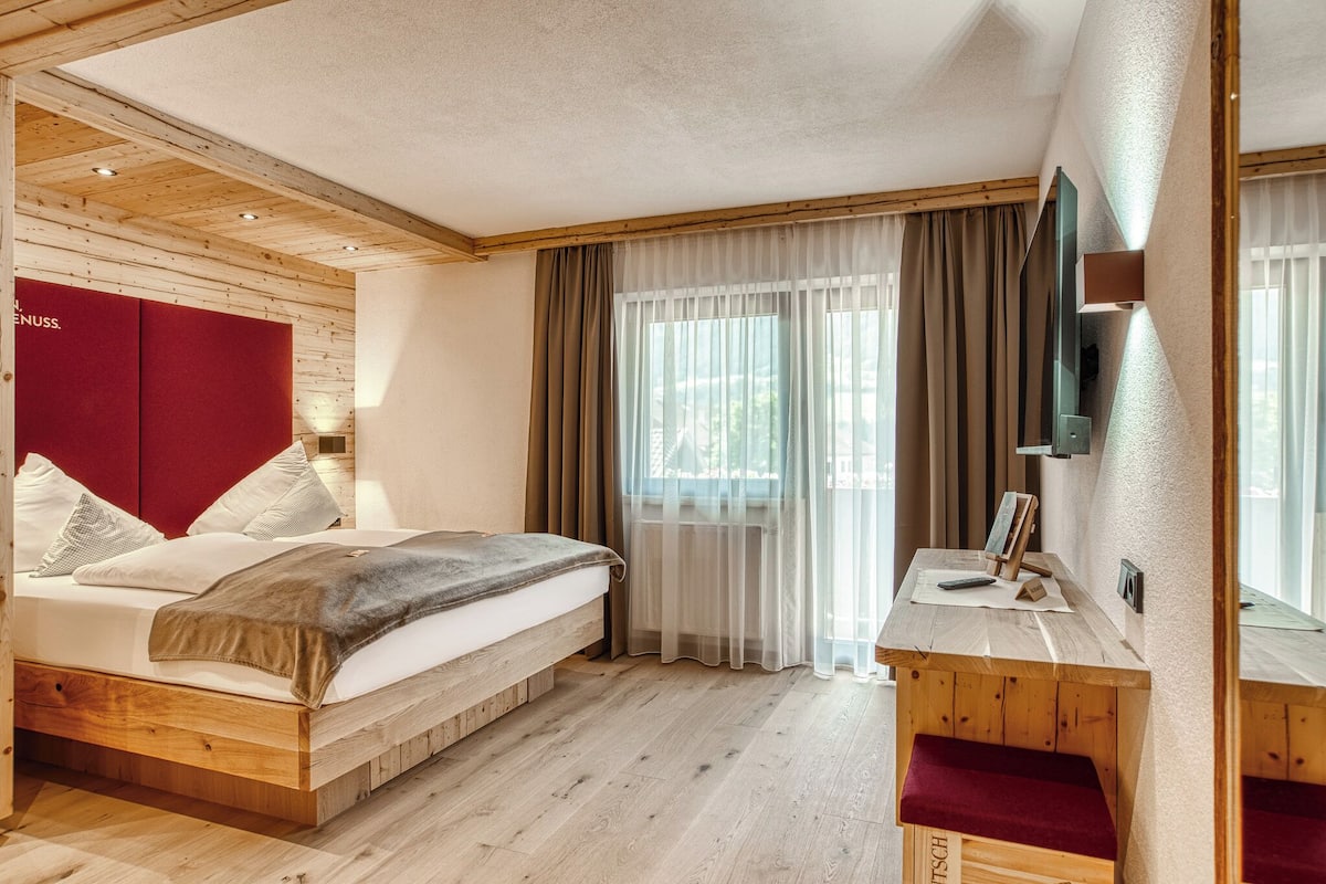 A wooden-framed room with a bed, a desk, and a television.