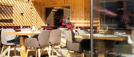A modern wooden interior with tables and chairs, large windows, and a visible fire extinguisher.