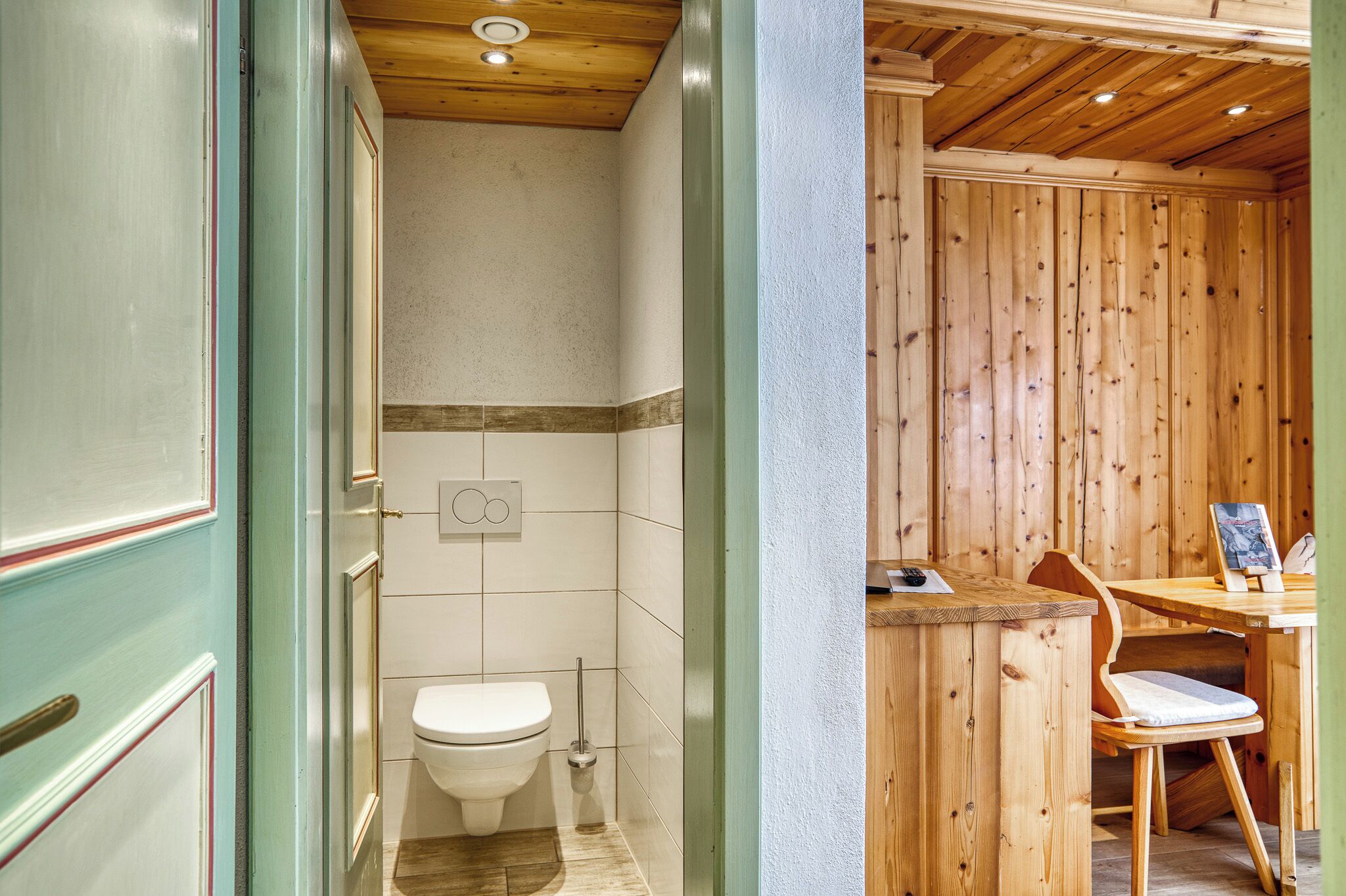 A wooden interior with a toilet, a small table with a chair, and a wooden partition.