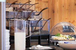 A buffet setup with various food items in transparent containers, a glass milk jug, and a cheese and fruit display under a dome. - Hotel Alpenstolz (Mieders)