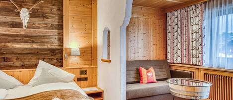 A wooden interior with a bed, a sofa, a glass table, and a wall-mounted deer skull.