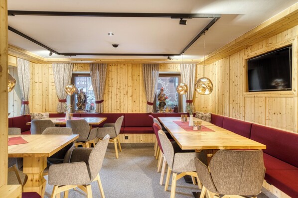 A wooden-paneled room with tables and benches, a large window, and a statue. - Hotel Alpenstolz (Mieders)