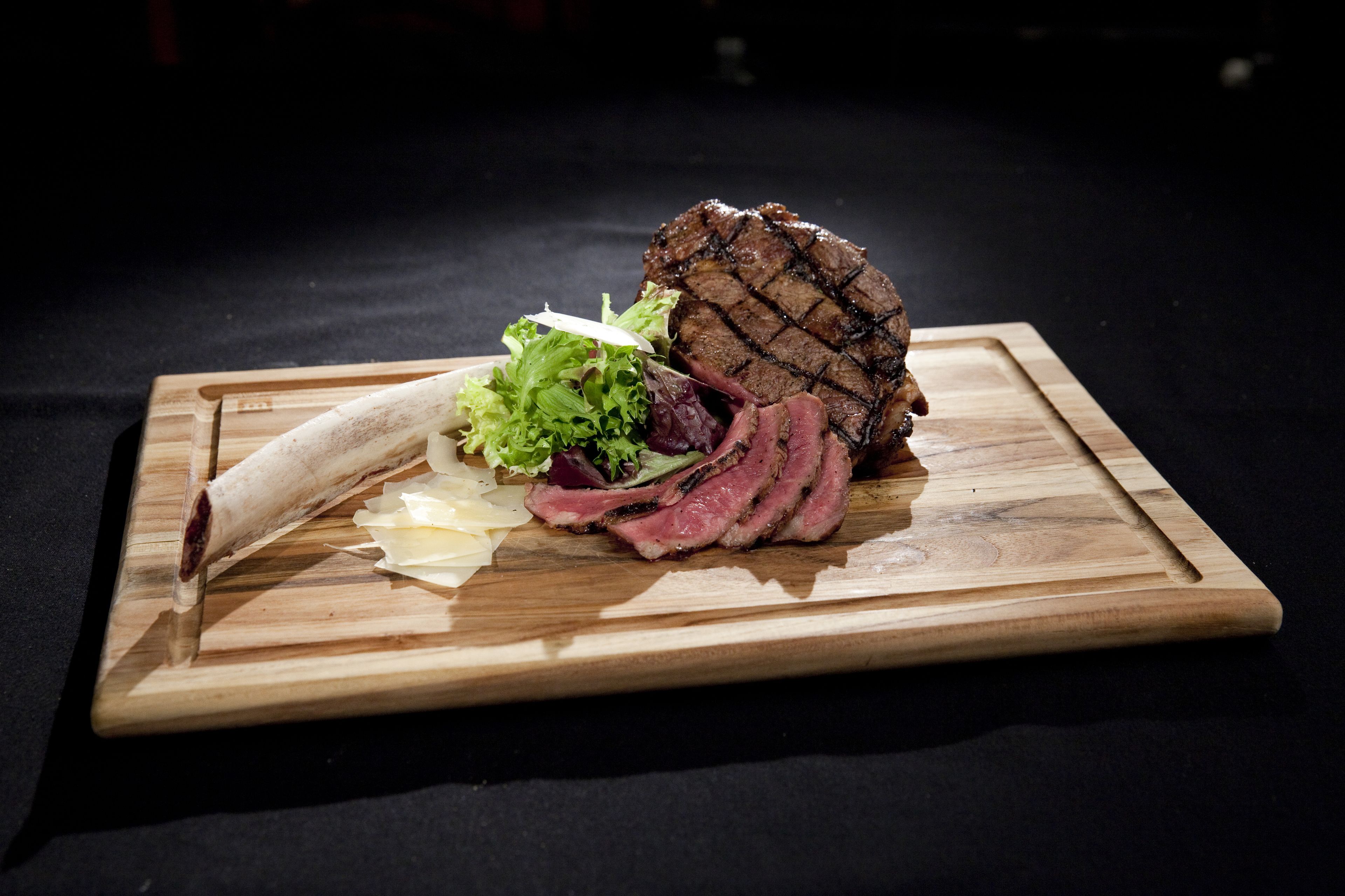 Un bife con marcas de parrilla, acompañado de lechuga y un trozo de queso sobre una tabla de madera.