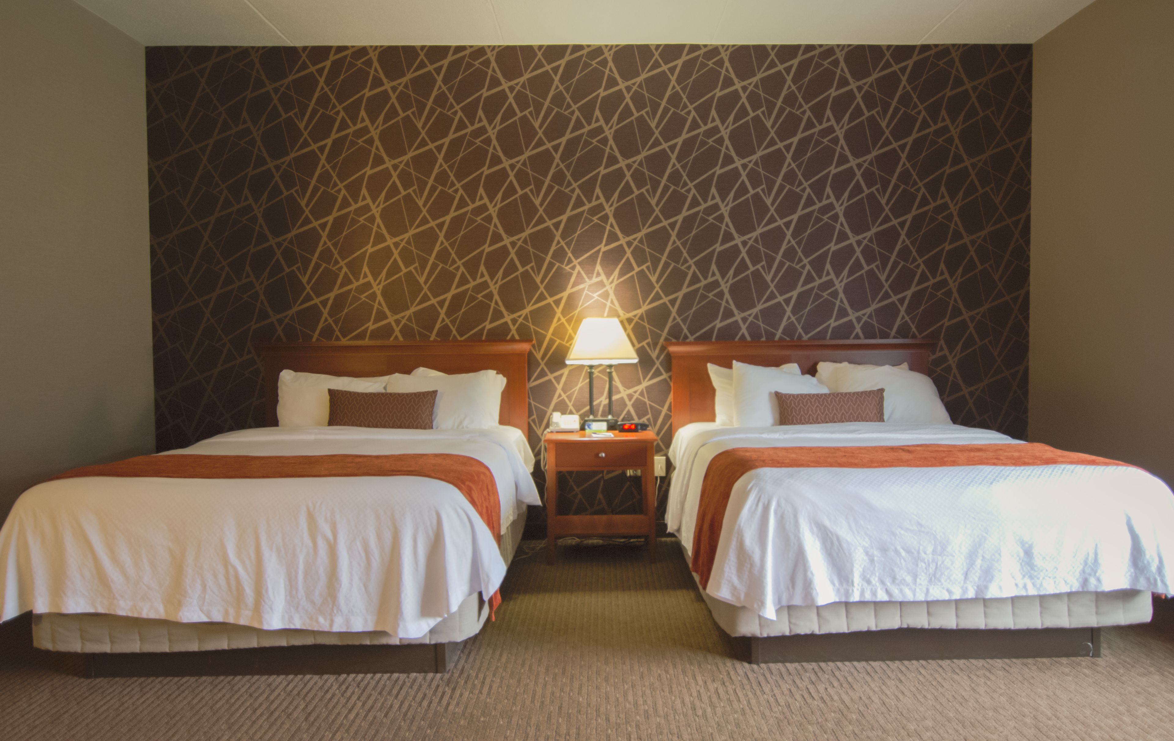 A hotel room with two beds, a nightstand with a lamp, and a patterned wall.