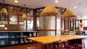 A restaurant with a large wooden table, red bar stools, and woven pendant lights. - WOT Sarrazola Soul (Sintra)