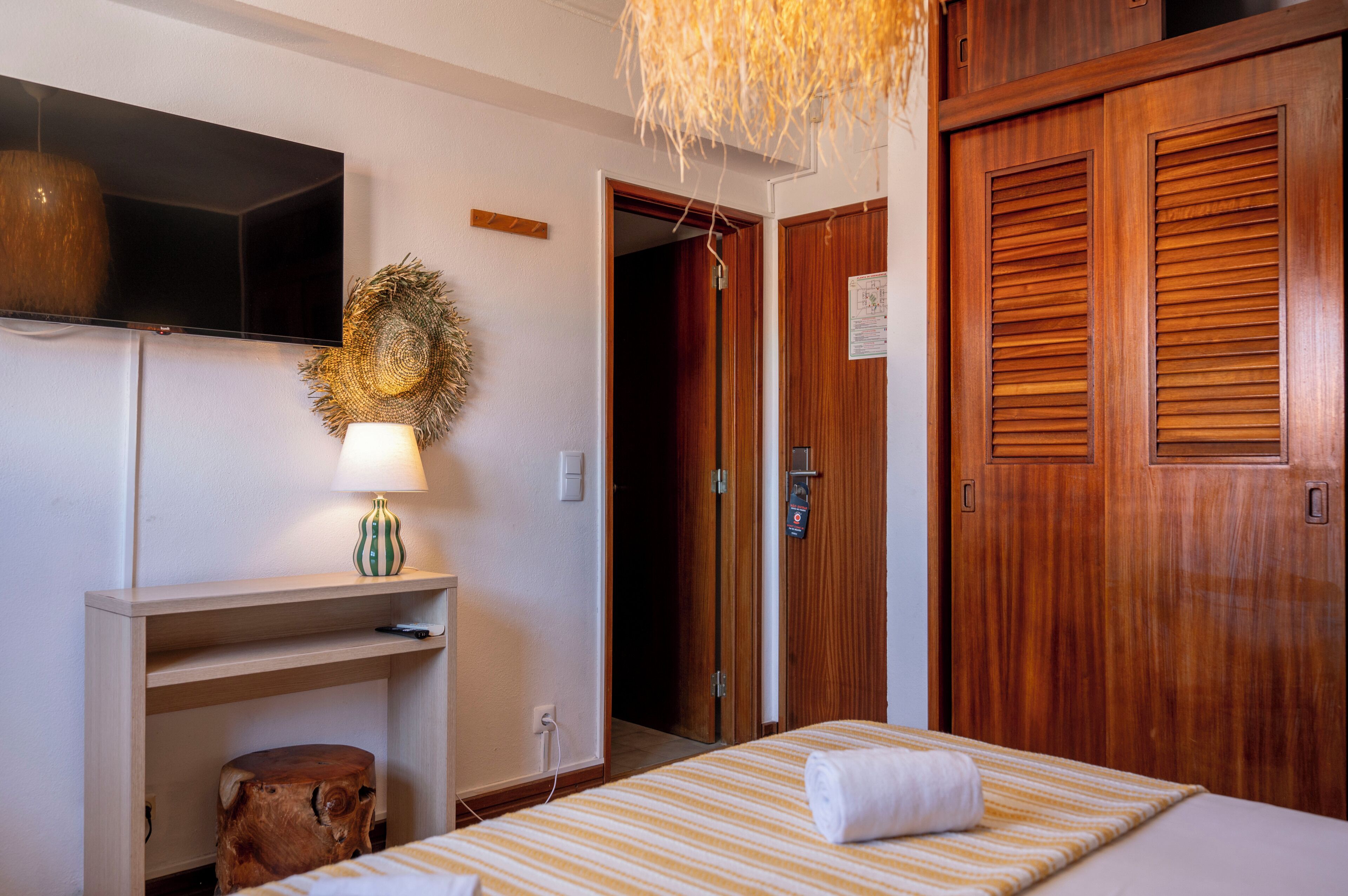A hotel room with a bed, a desk, a television, and a wooden door.