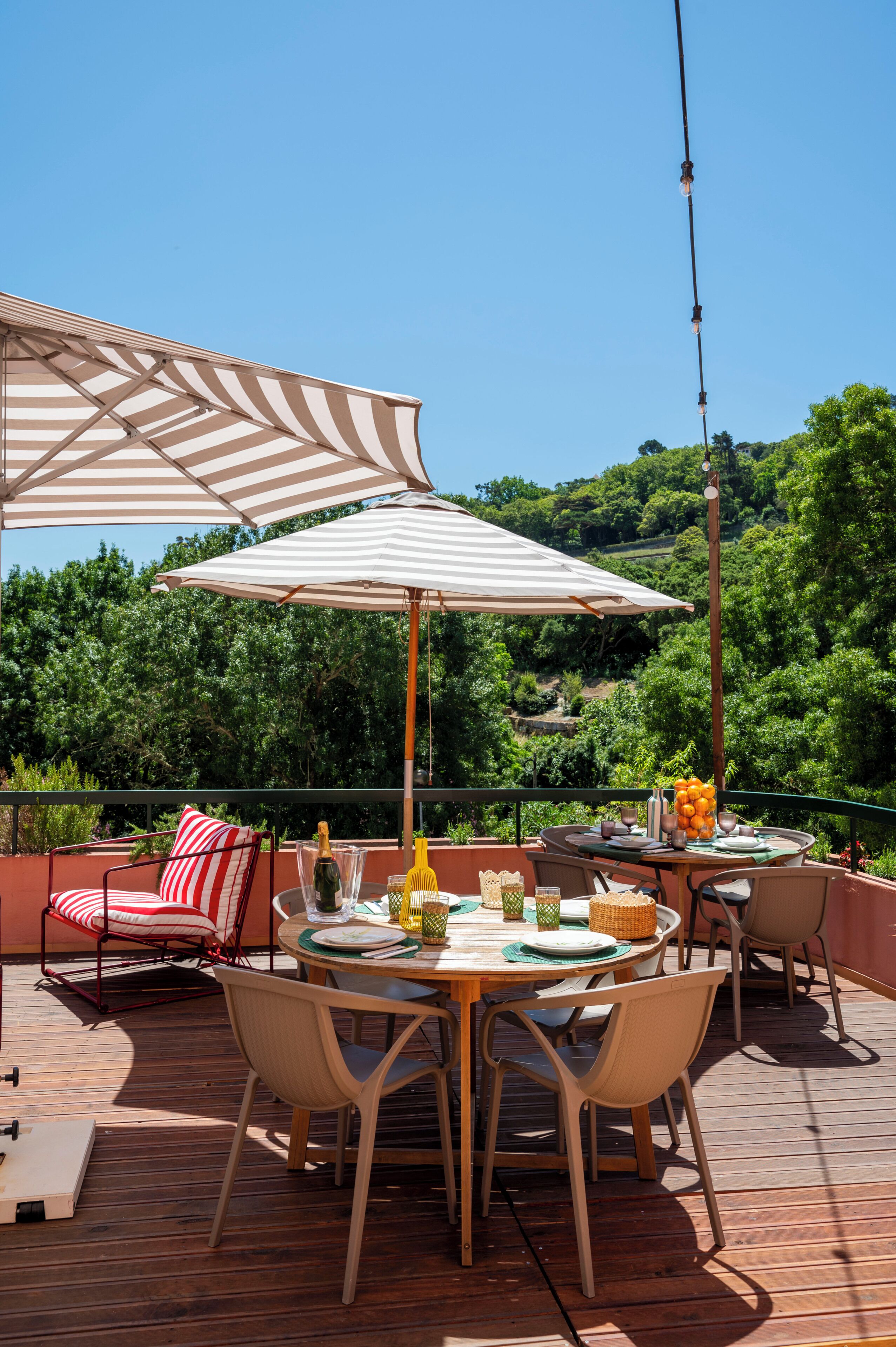 An outdoor dining area with striped umbrellas, wooden deck, and a view of green hills.