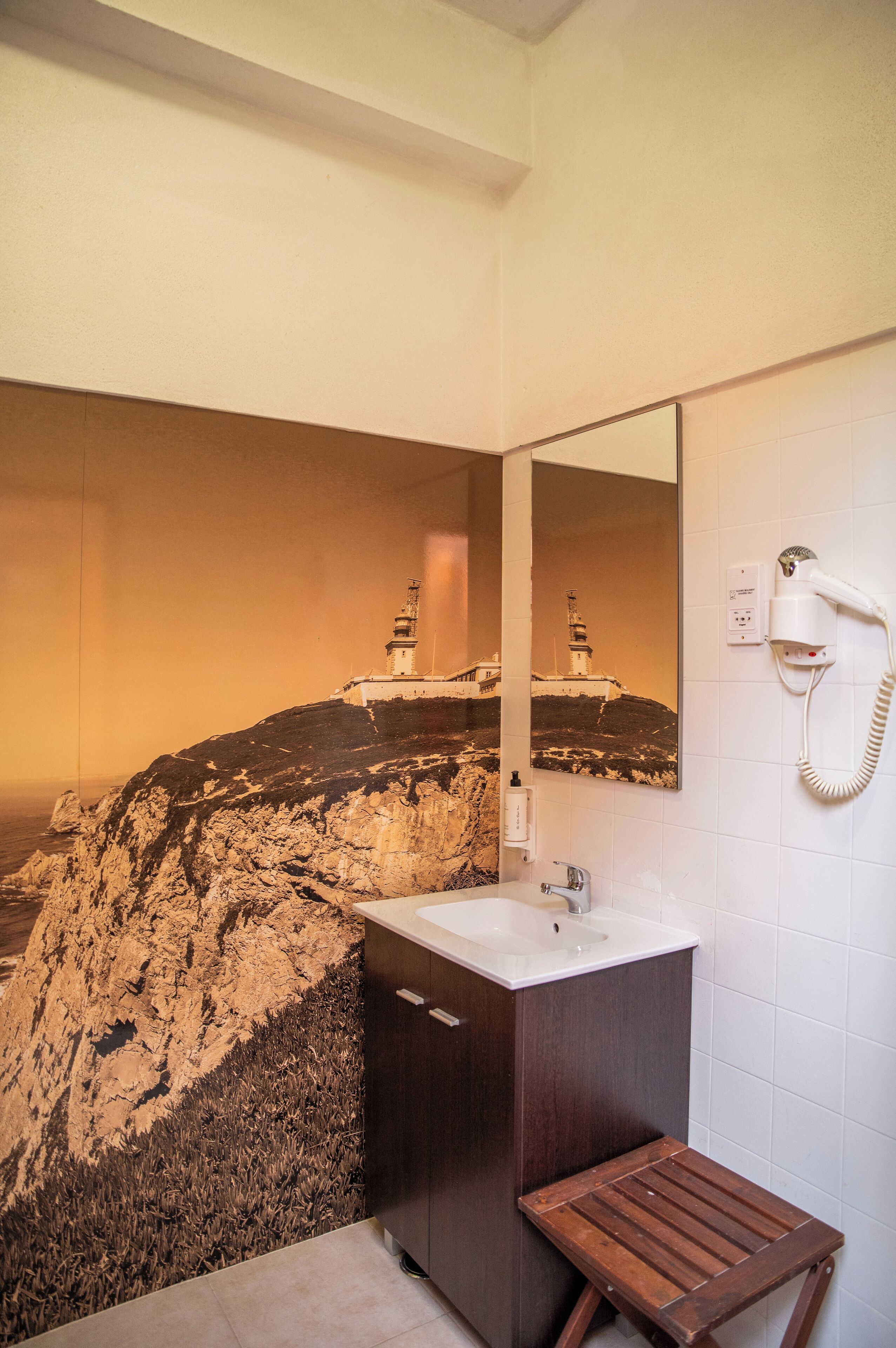 Een badkamer met een wastafel, spiegel en een haardroger aan de muur.