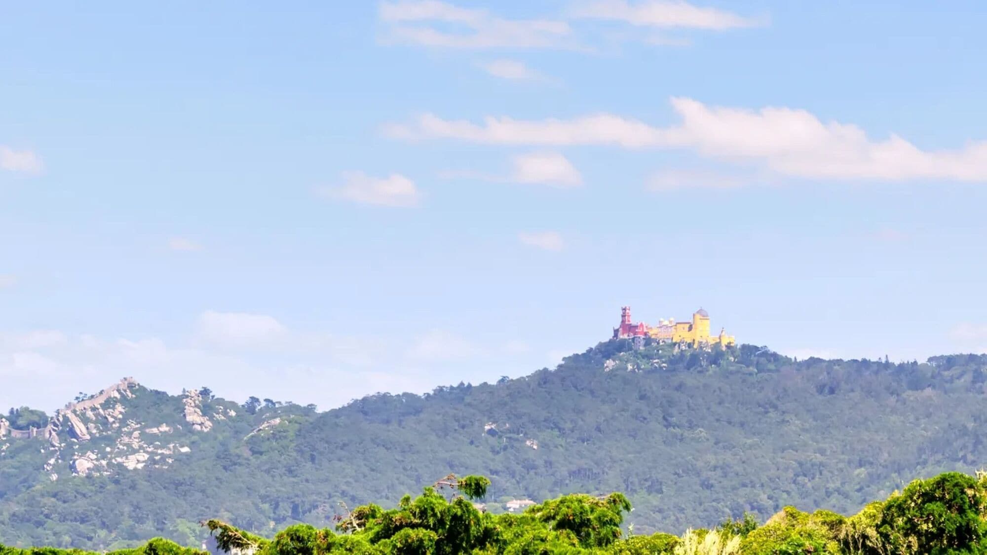 A hilltop building with a prominent tower, surrounded by lush greenery and a clear sky.