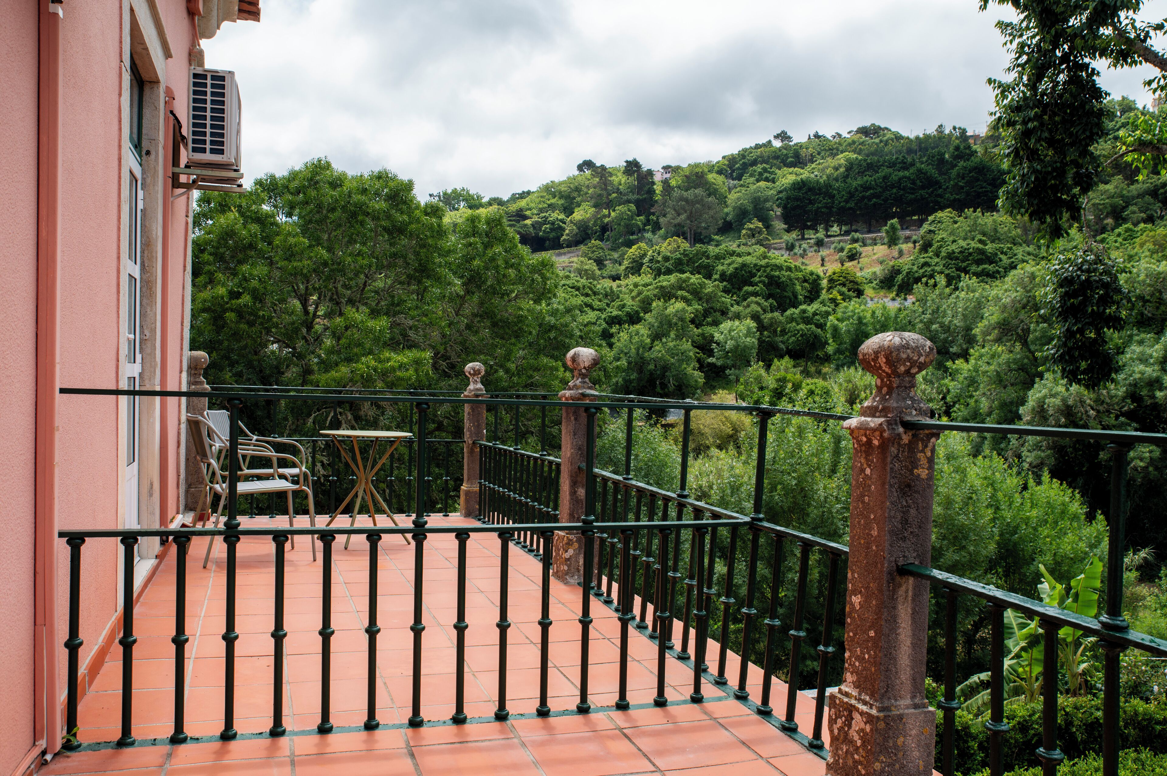 A balcony with a tiled floor, a metal railing, and a view of a lush green landscape.