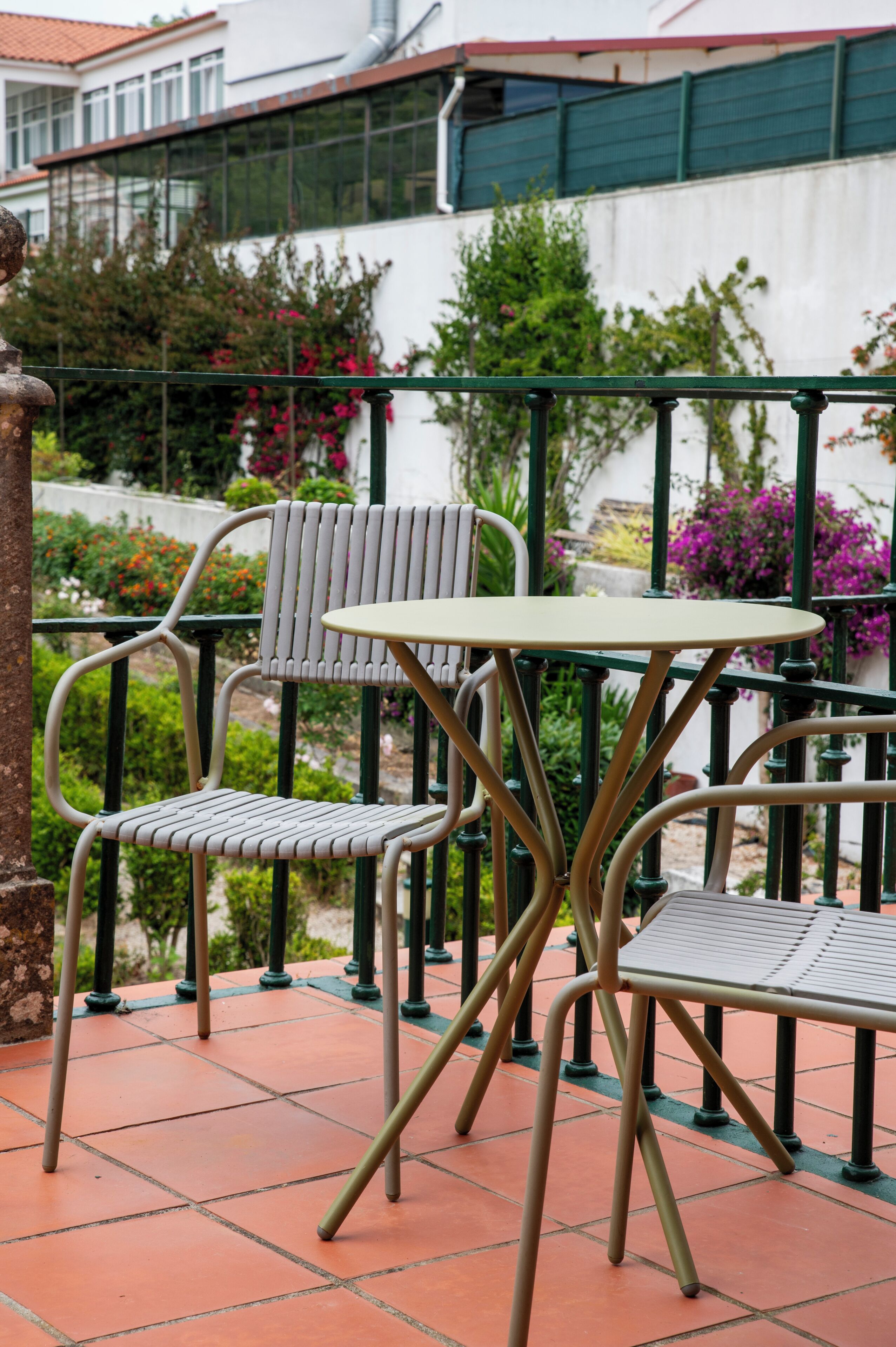 A terrace with a table and chairs, surrounded by a railing and potted plants.