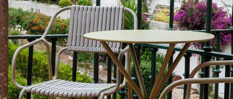 A terrace with a table and chairs, surrounded by a railing and potted plants.