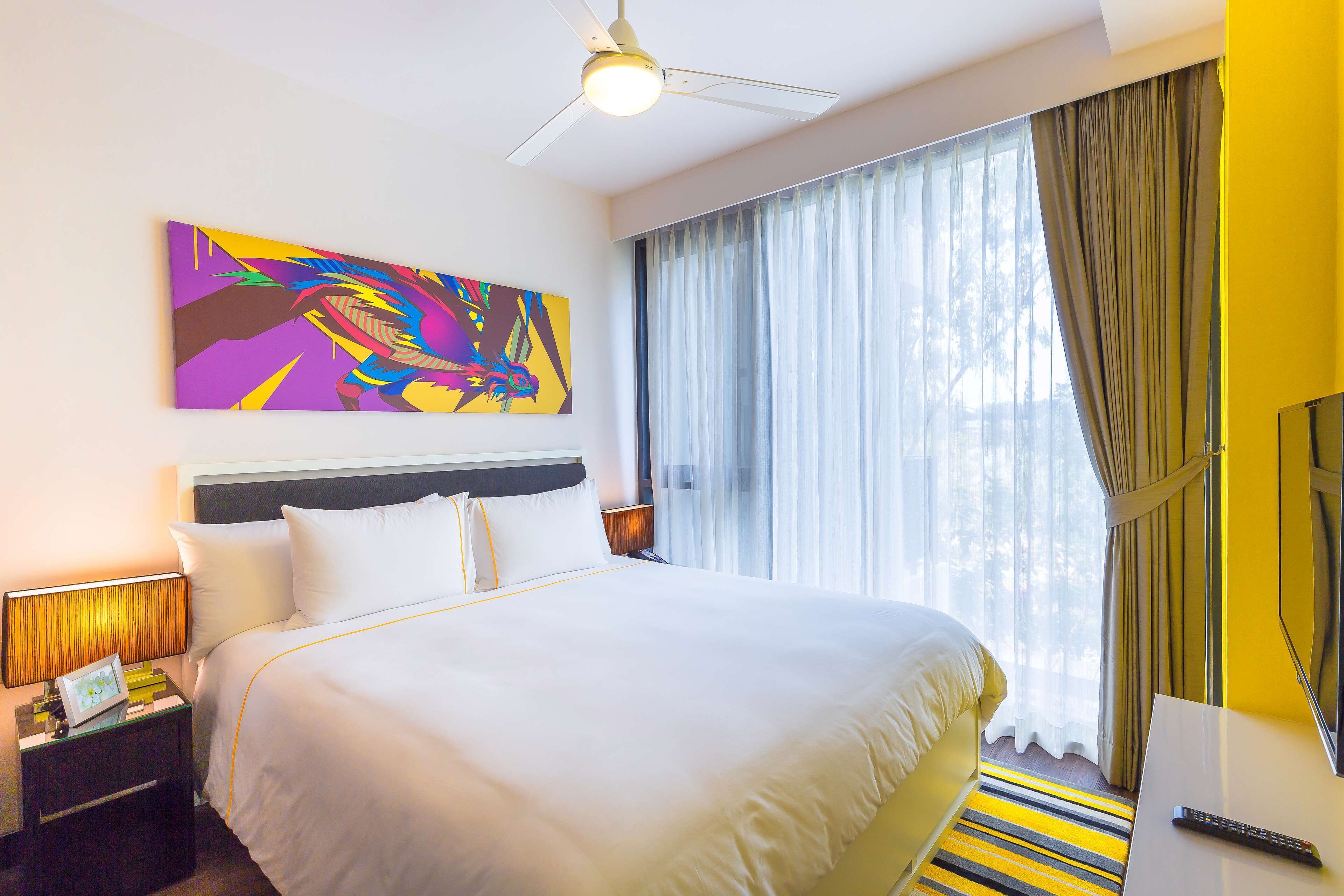 Una camera d'albergo con un letto, un comodino, una lampada, un quadro e una finestra con tende.