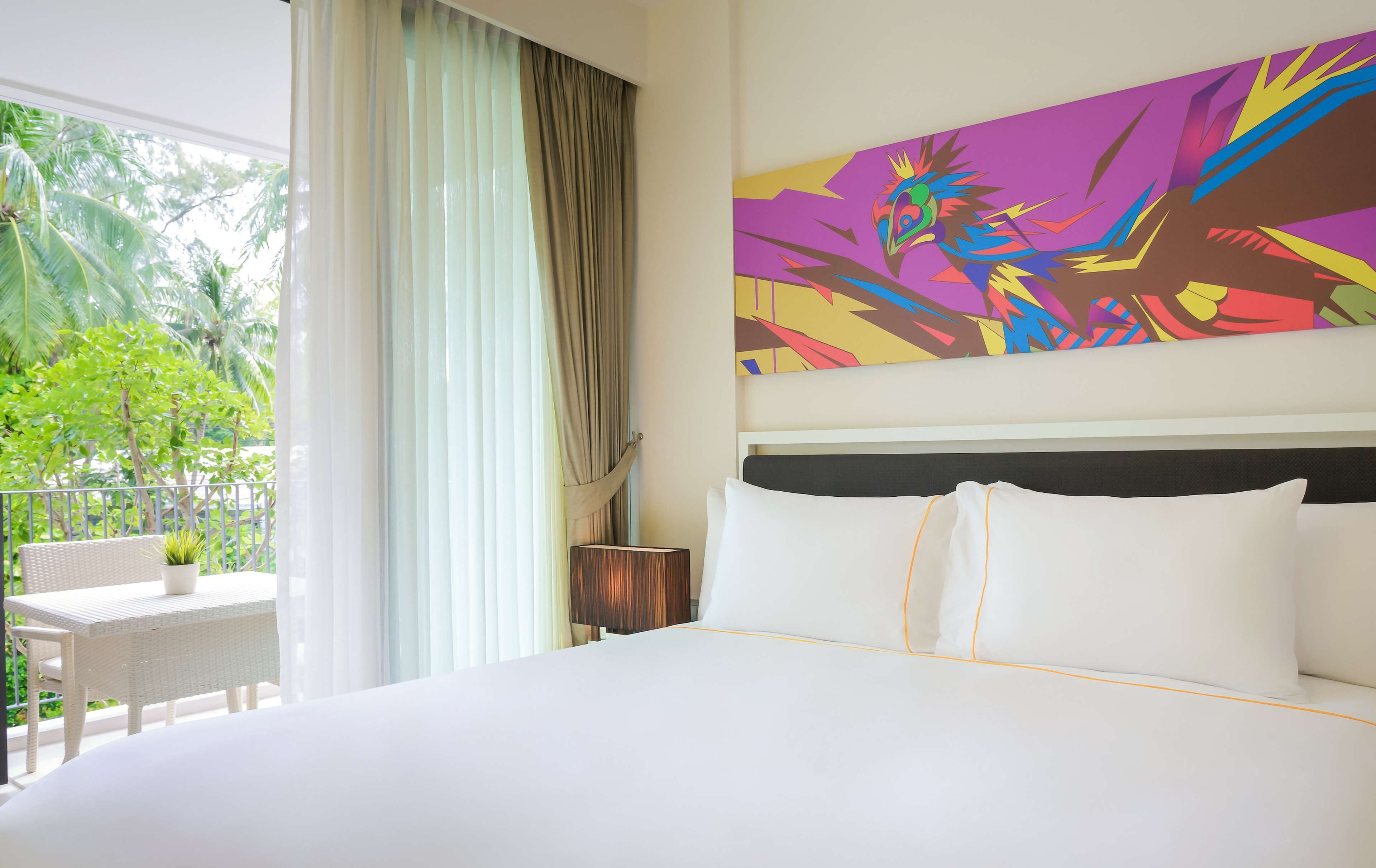 Habitación de hotel con una cama grande, vistas a palmeras y un cuadro abstracto de colores en la pared.