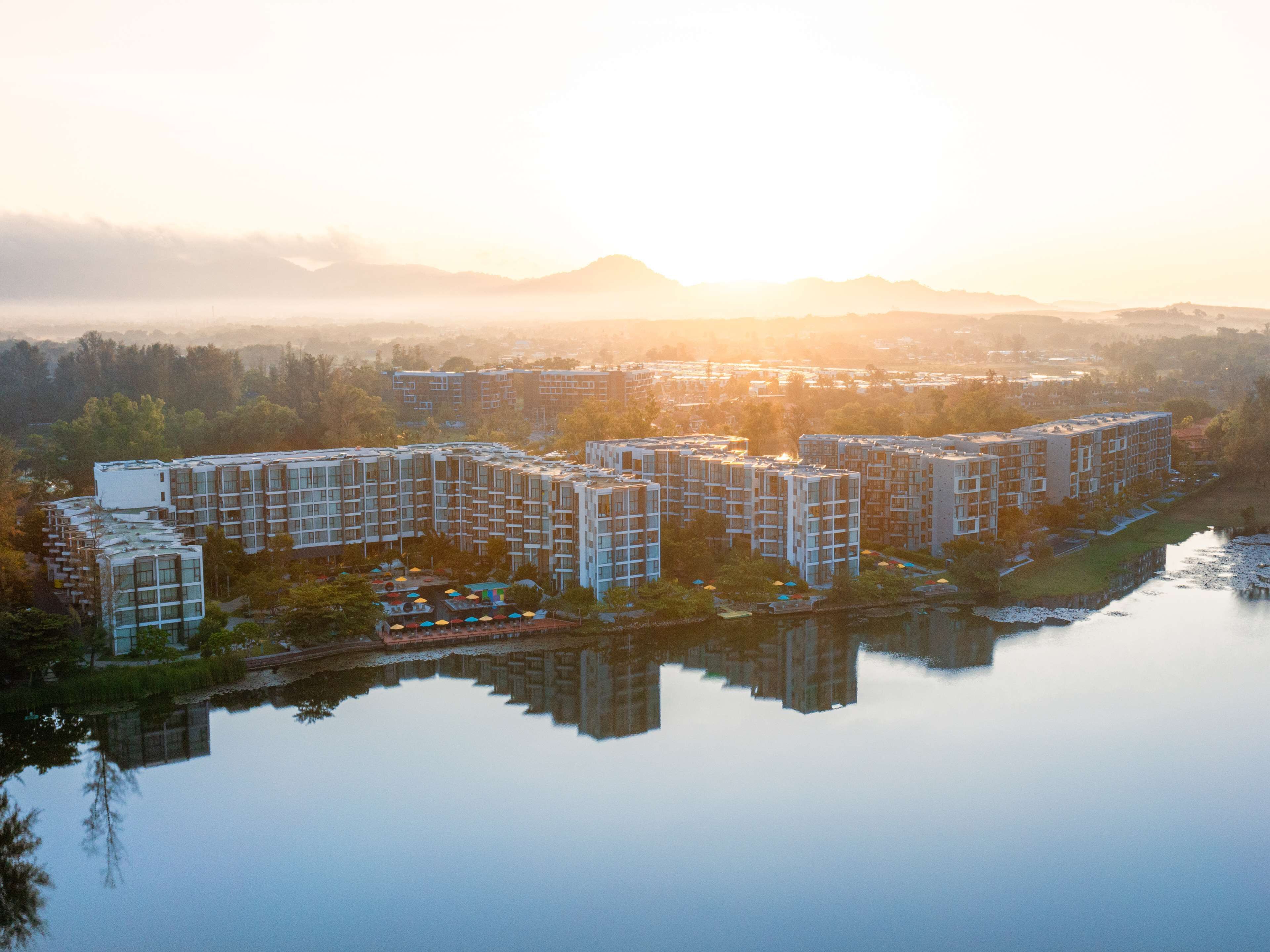 Un ensemble immobilier résidentiel de grande hauteur, composé de plusieurs étages, entouré de verdure et bordé par un plan d’eau dans lequel se reflètent les bâtiments.
