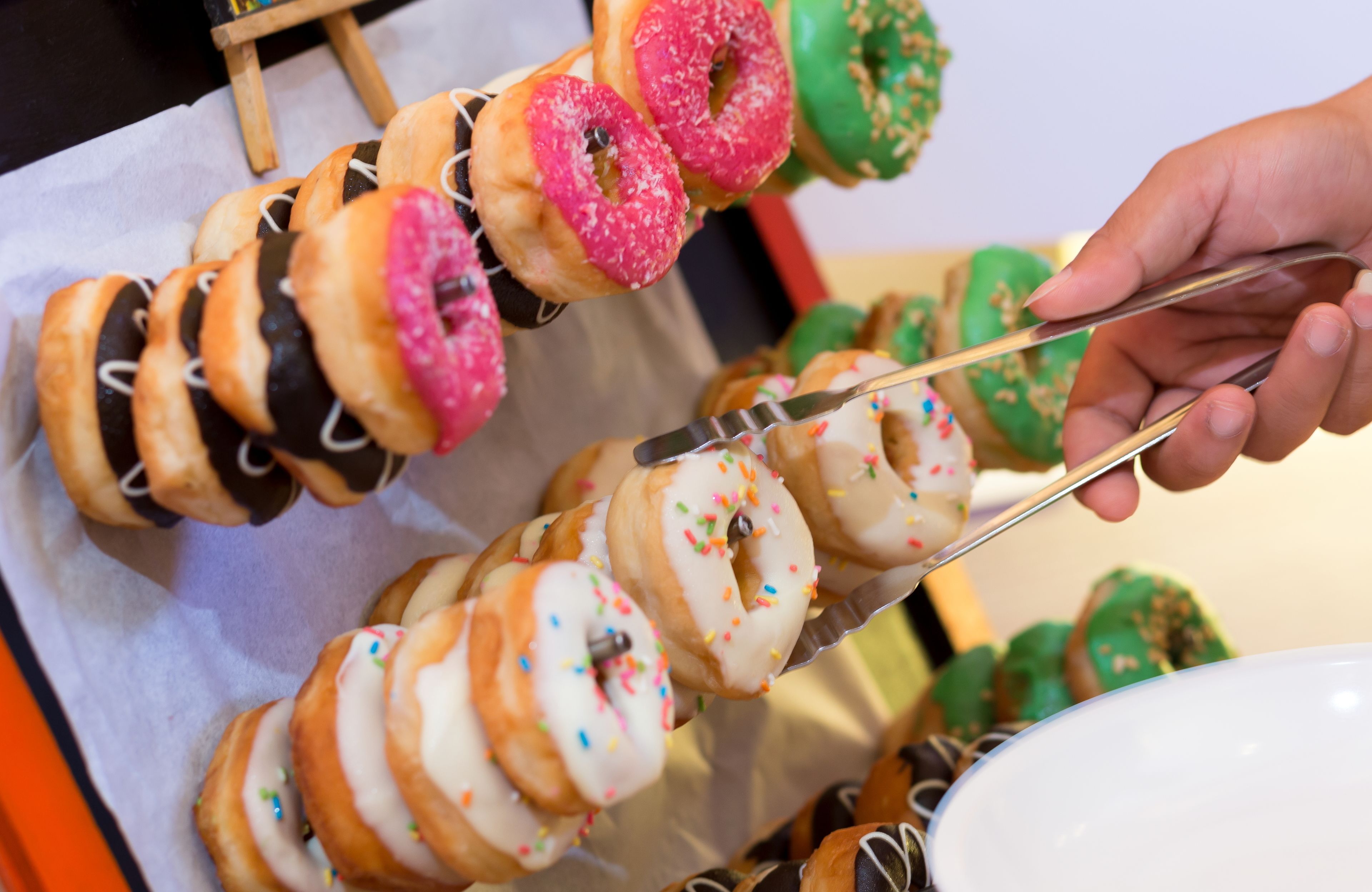 A hand holding tongs with a skewer of donuts.