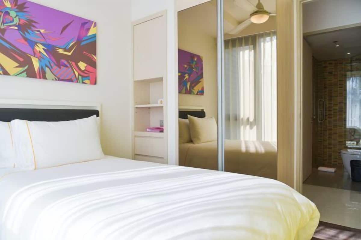 A hotel room with a bed, artwork on the walls, a sliding door, and a bathroom visible through the door.