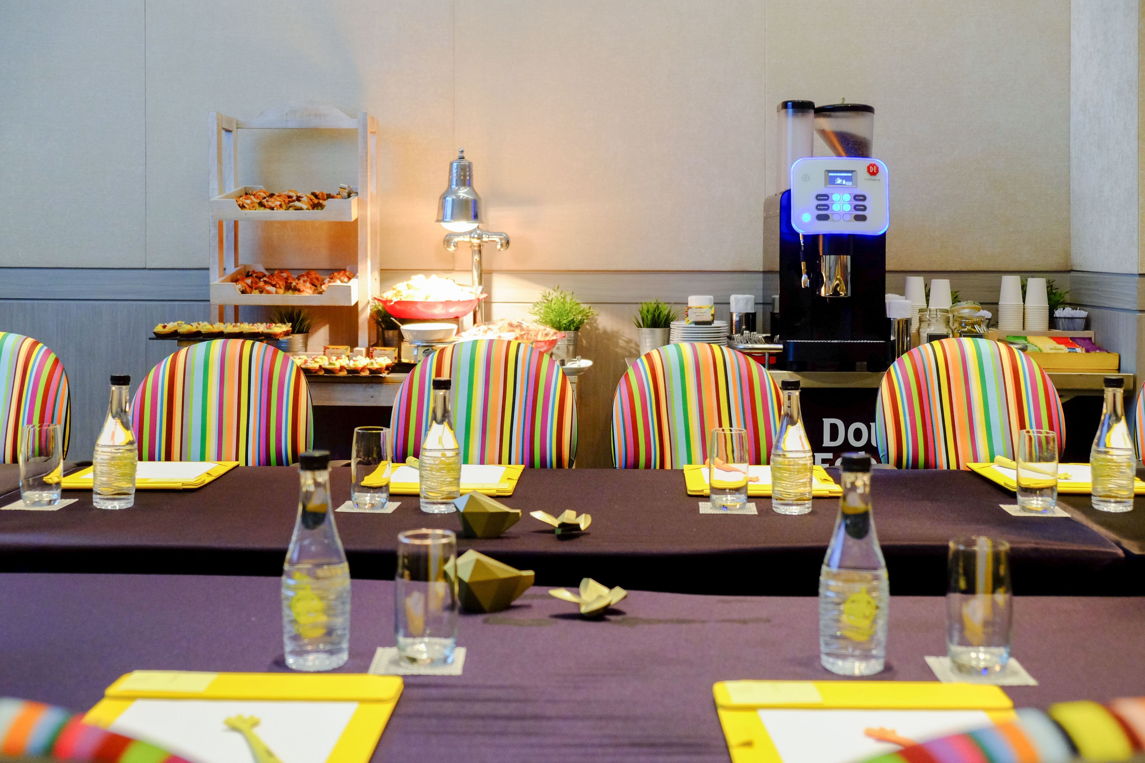 A conference room with striped chairs, a buffet table with food, and a coffee machine.