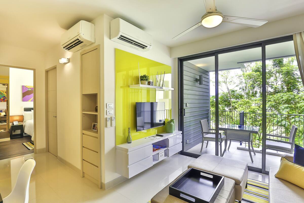 A modern living room with a flat-screen TV, a bright green accent wall, and a balcony with outdoor furniture.