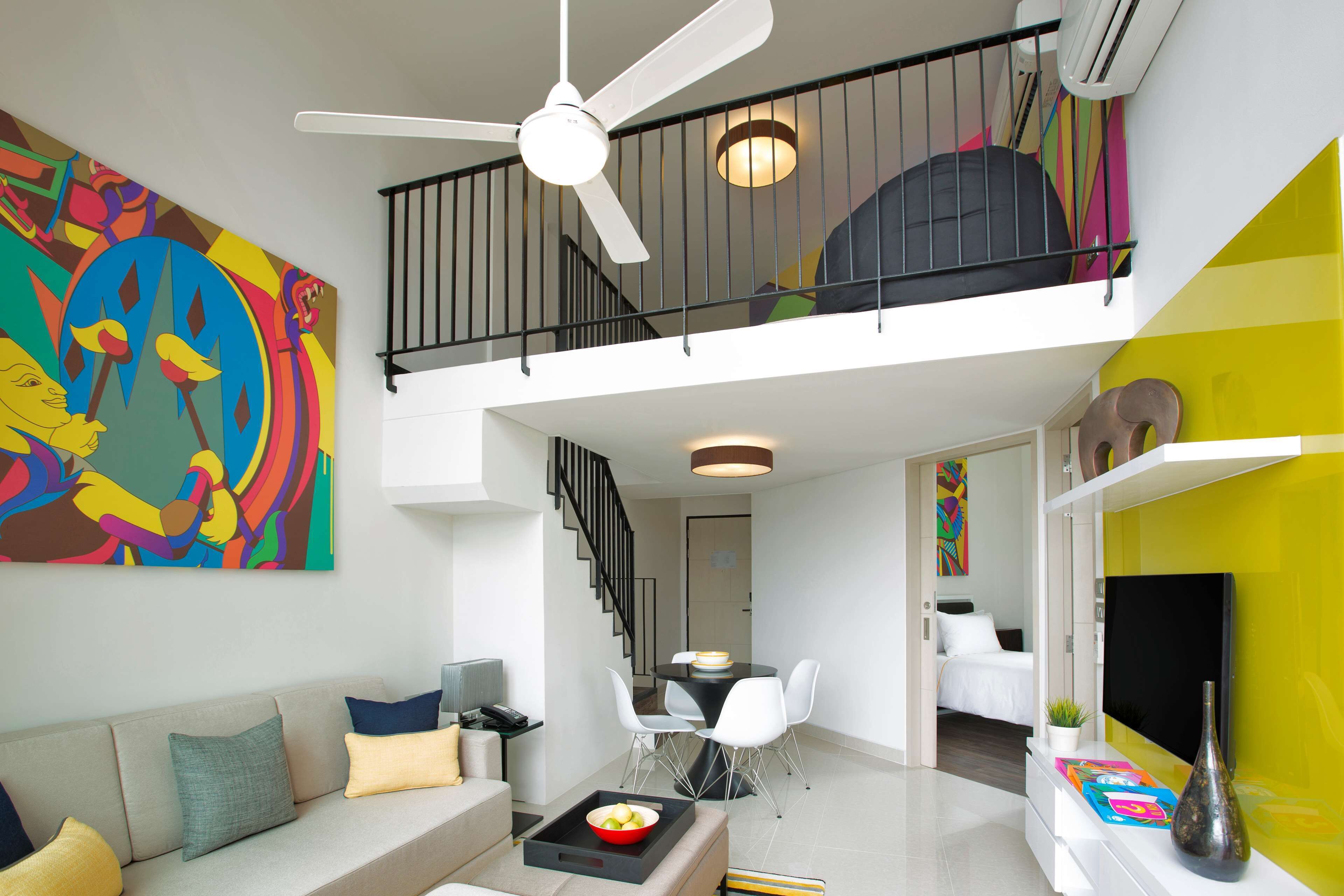 Un interior moderno con una escalera que conduce a un nivel superior, un comedor con mesa y sillas, y una sala de estar con sofá y un cuadro abstracto de gran tamaño.