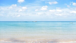 Una playa con agua cristalina y un barco a lo lejos.