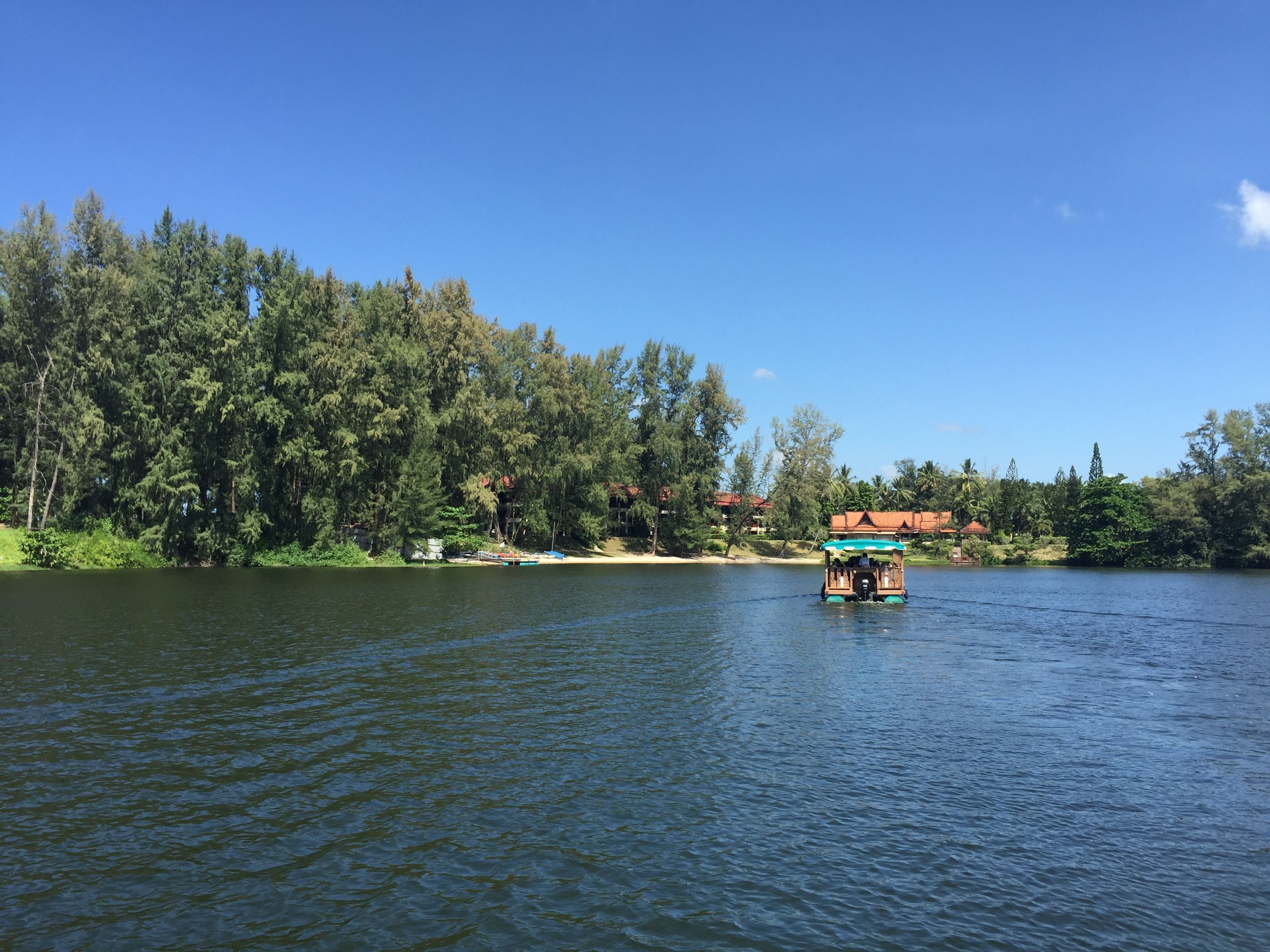 A boat on a calm lake with a forested shoreline and a building in the background.