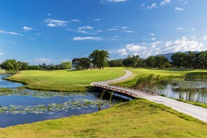 Ein Golfplatz mit einer Brücke über einem Teich, umgeben von üppigem Grün und Bäumen.