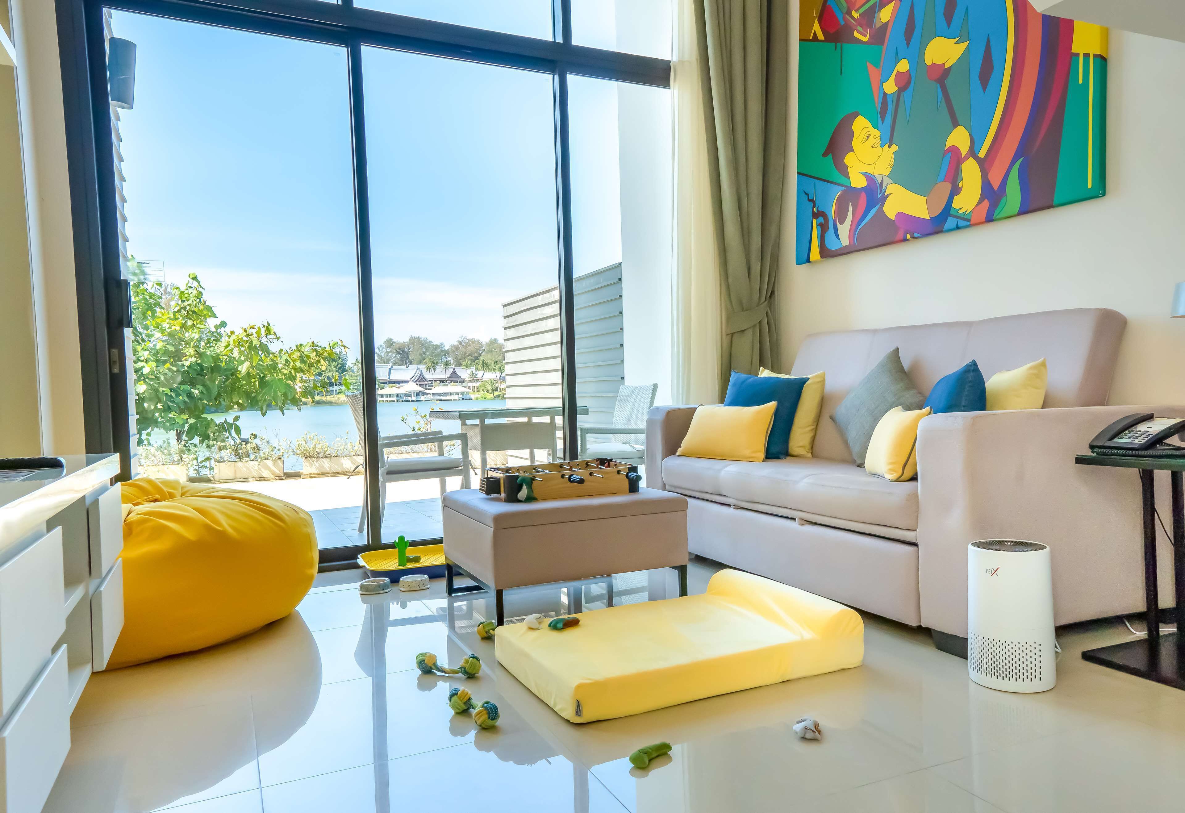 A modern living room with a sofa, ottoman, and a large window offering a view of the sea.