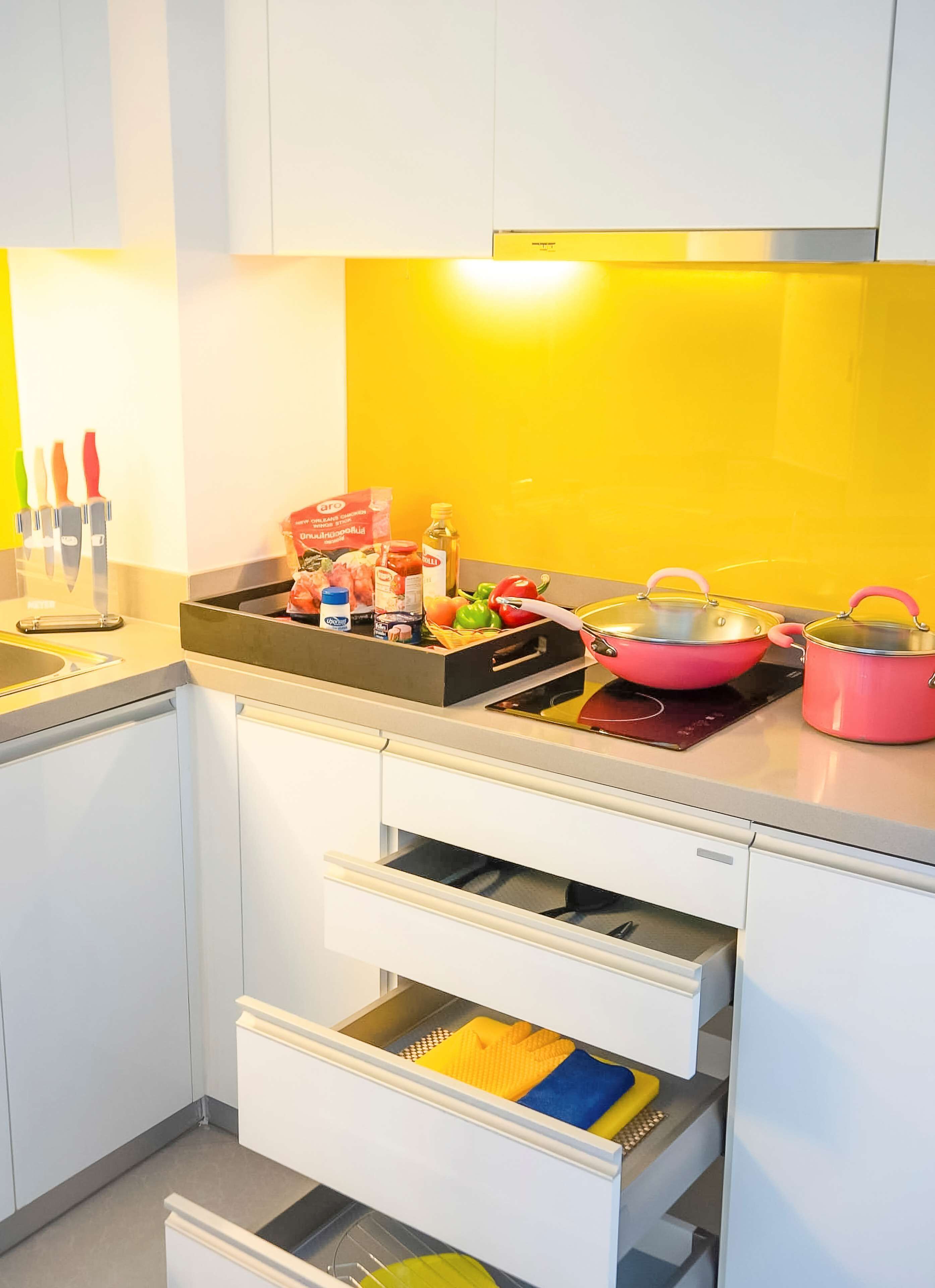 Una cocina moderna con armarios blancos, salpicadero amarillo y varios utensilios de cocina sobre la encimera.