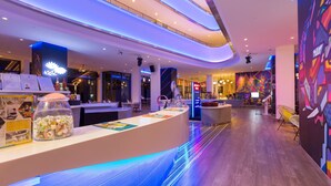Un vestíbulo de hotel moderno con un mostrador de recepción curvo, un recipiente de vidrio con aperitivos y un mural de colores en la pared.