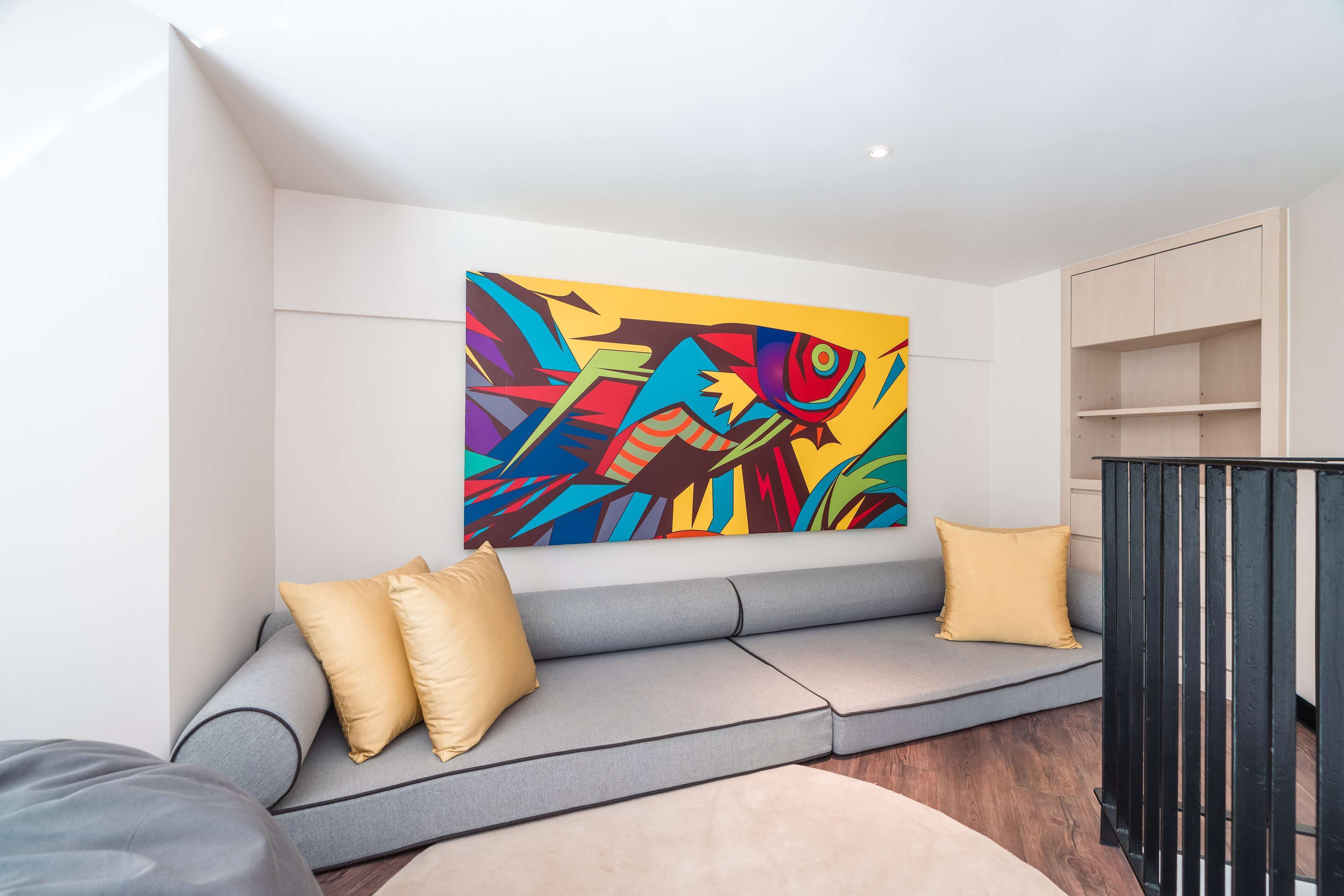 A modern living room with a grey sofa, two yellow cushions, and a colorful abstract painting on the wall.