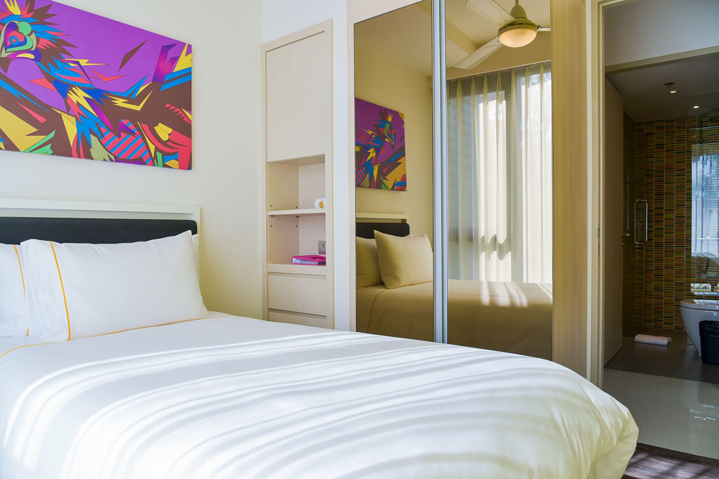 A hotel room with a large bed, a bedside table, a mirror, and a bathroom visible through an open door.