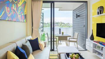 A modern living room with a sofa, a coffee table with fruit, a TV, and a balcony with a table and chairs.