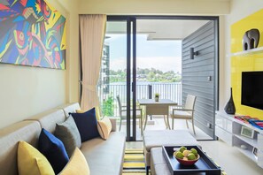 A modern living room with a sofa, a coffee table with fruit, a TV, and a balcony with a table and chairs. - Cassia Phuket, part of Banyan Group (Choeng Thale)