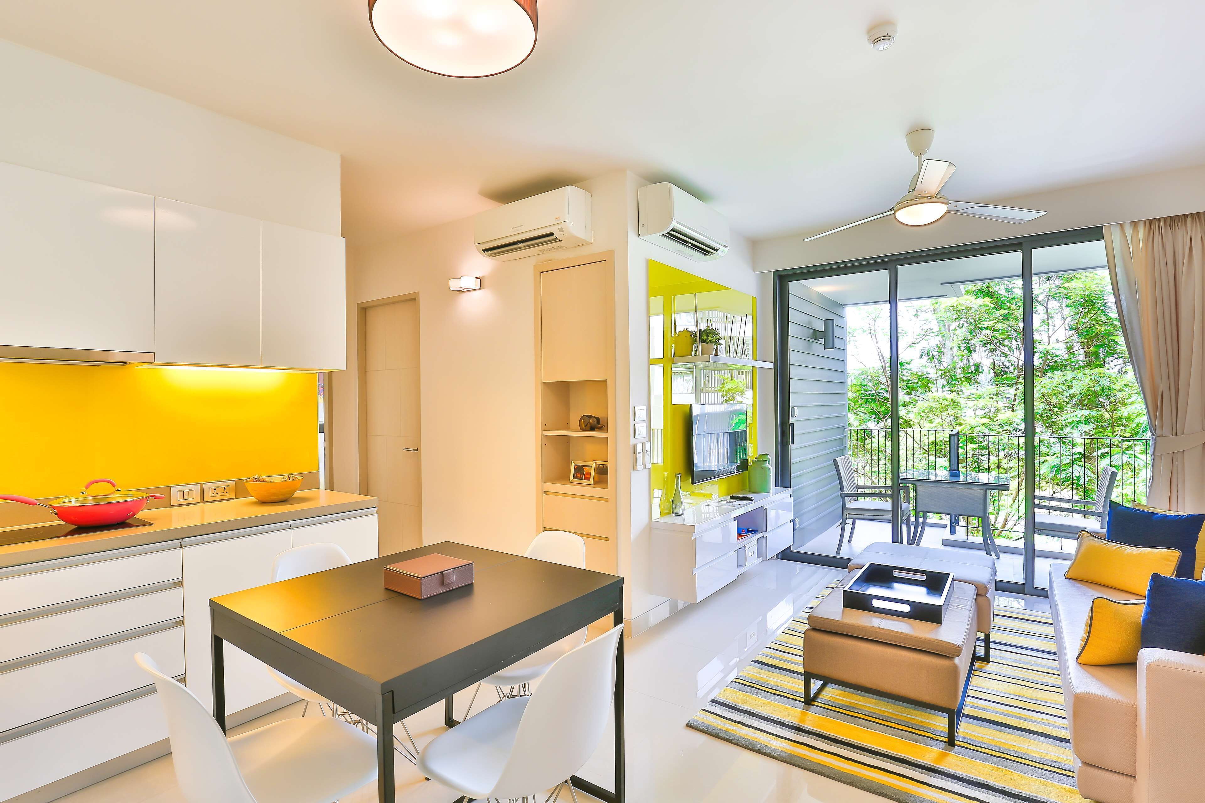 A modern kitchen with white cabinets, a dining area with a table and chairs, and a living room with a sofa and a view of greenery outside.