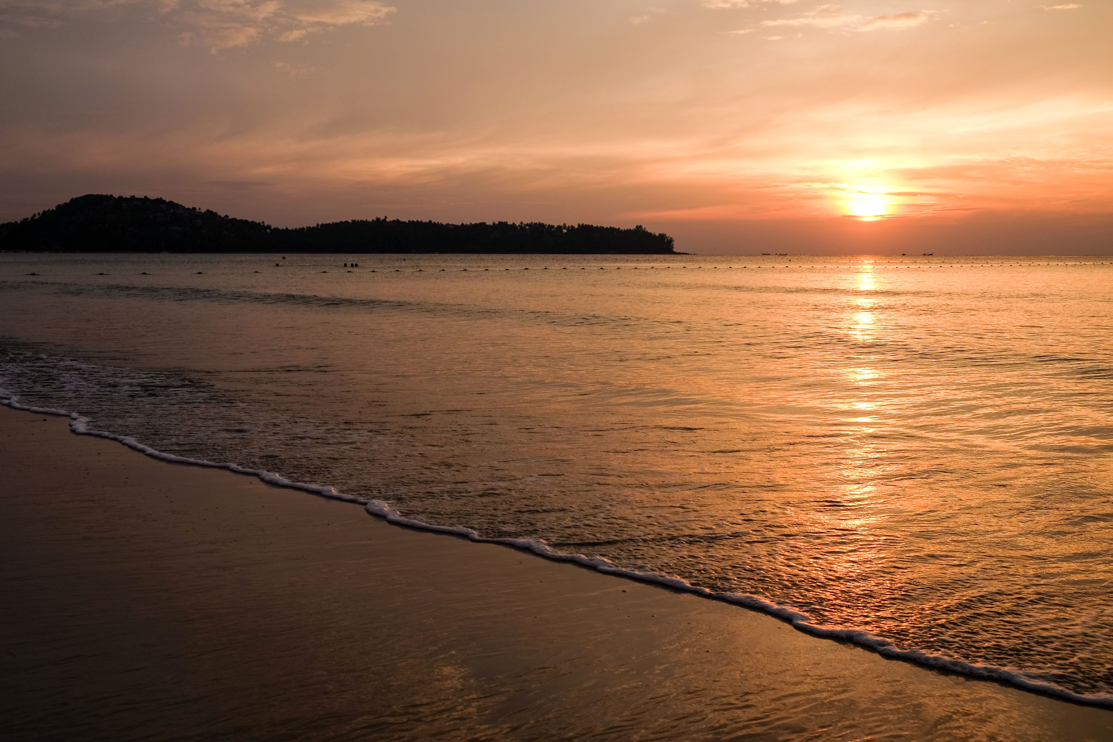A beach at sunset with calm waters and a distant landmass.