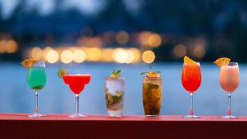 A row of five colorful cocktails on a red surface with a blurred cityscape in the background.